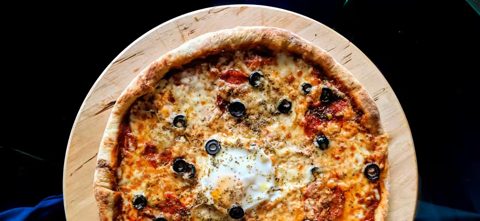 Baked Pizza with Tomatoes, Cheese, Olives, Salami, and a Fried Egg